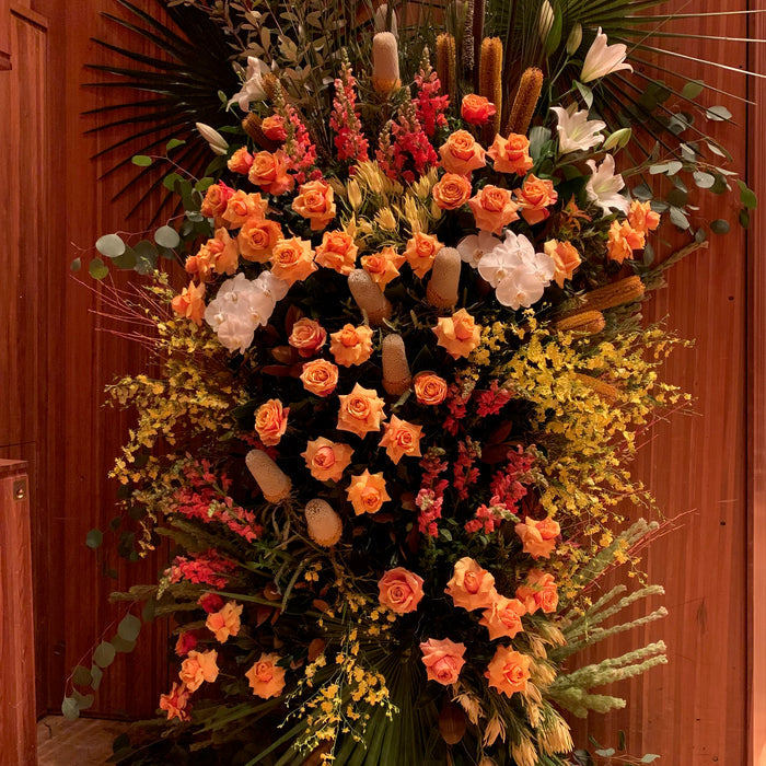 Orange roses, white flowers and foliage in a memorial floral arrangement