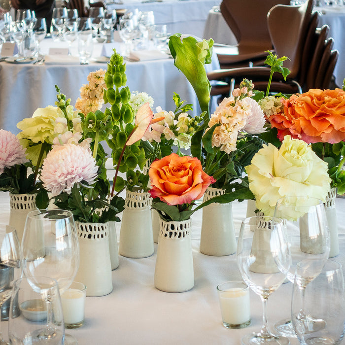 Colourful table flowers in white vessels individually made by Frankie’s mother for guests to take home