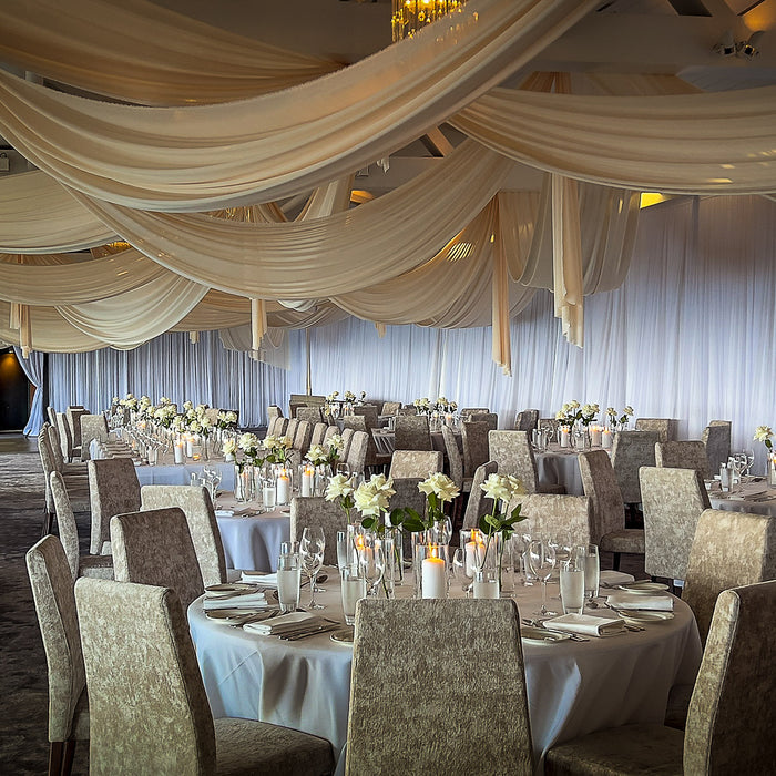 White ceiling draping above a wedding reception with pale flowers and candles
