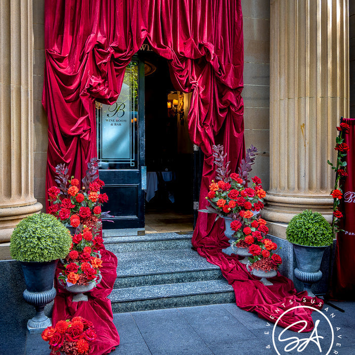 Bambini Trust exterior with burgundy draping and red floral urns framing the entrance