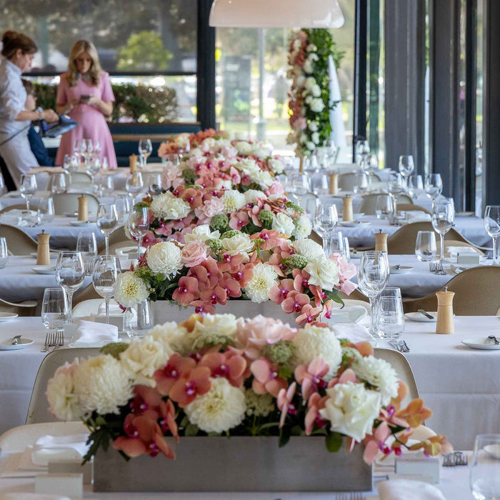 Pink and cream flower arrangements running along a wedding reception table
