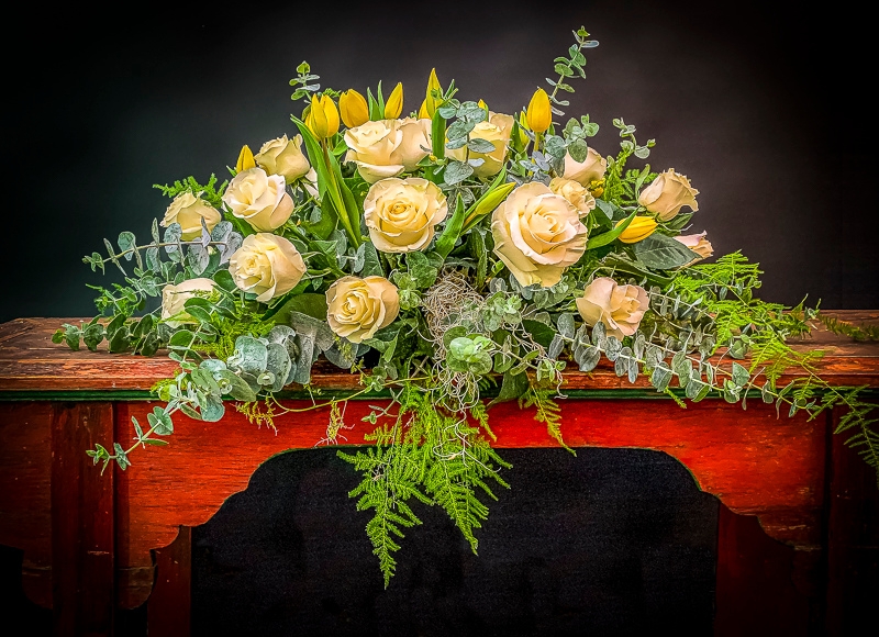 Compact casket cover in yellows featuring Australian eucalyptus, along with Spanish moss, roses and tulips